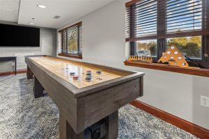 Shuffleboard table in the game room at Cedar Crest Retirement Community with window view and casual seating