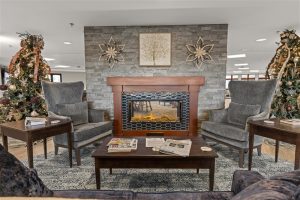 Inviting lounge area at Waterford Place Apartments featuring a cozy fireplace, elegant gray armchairs, holiday decor, and a warm, welcoming atmosphere.