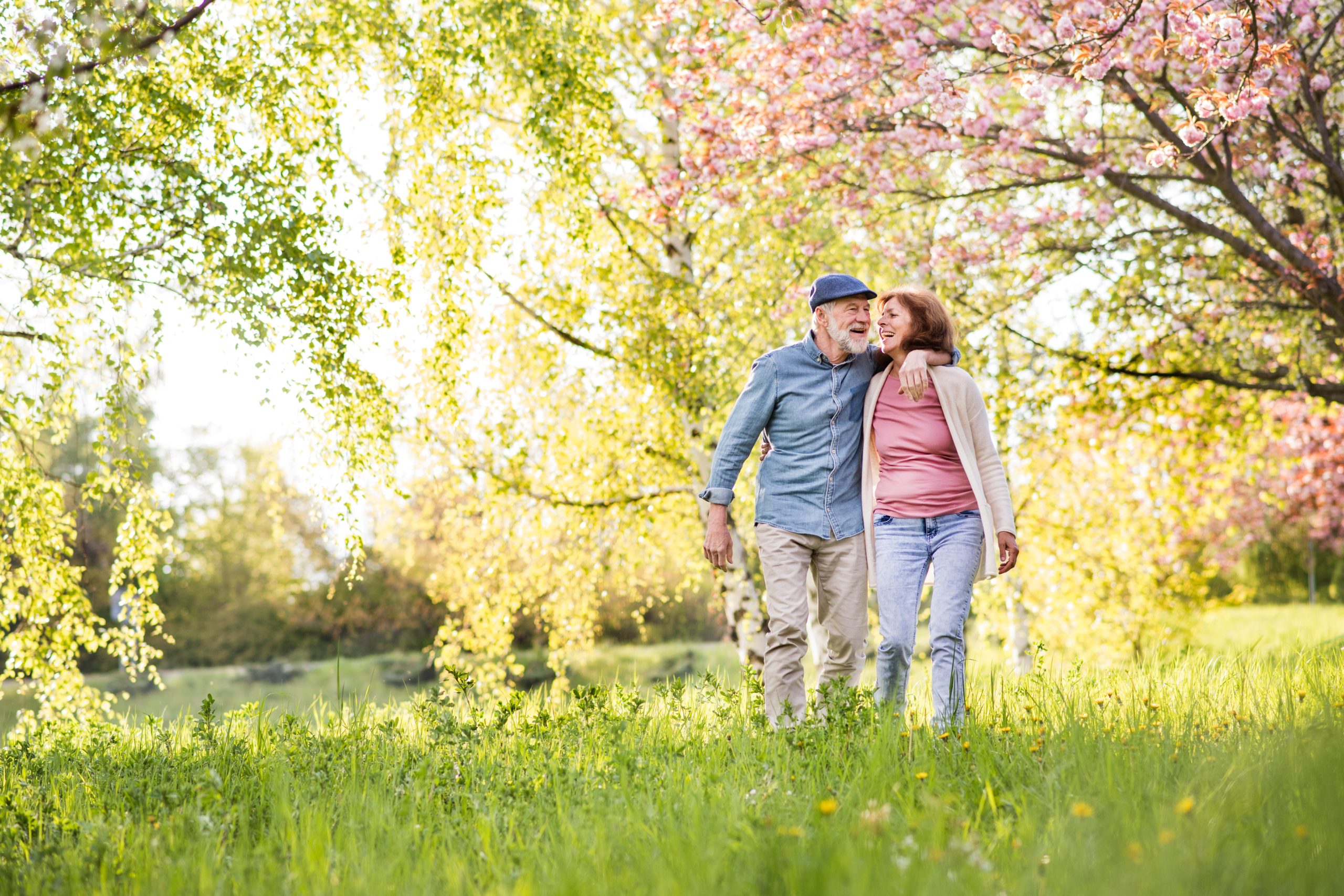 Senior couple walking outside in the spring with blooming trees and green meadow grasses