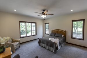 Large open bedroom with three windows and ceiling fan